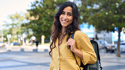 A young woman carrying a backpack is in a city plaza on a summer day.
