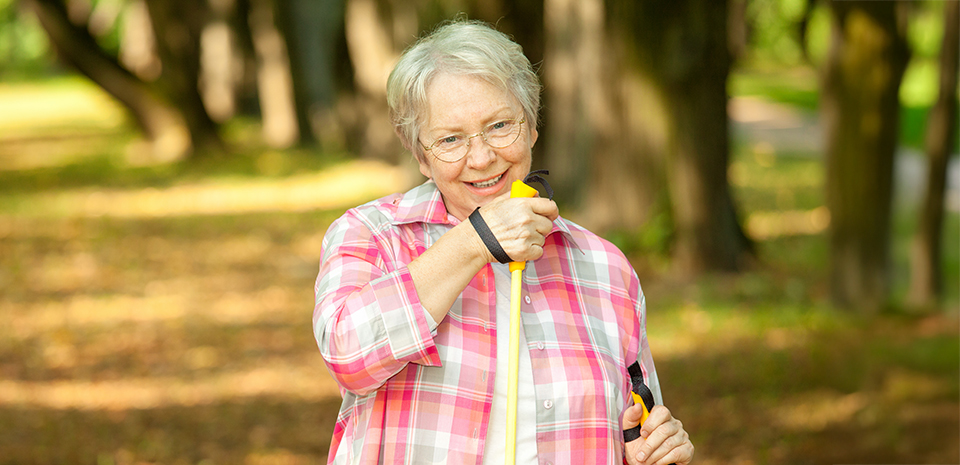 A senior woman uses walking sticks to prevent falls during her walk in the woods.