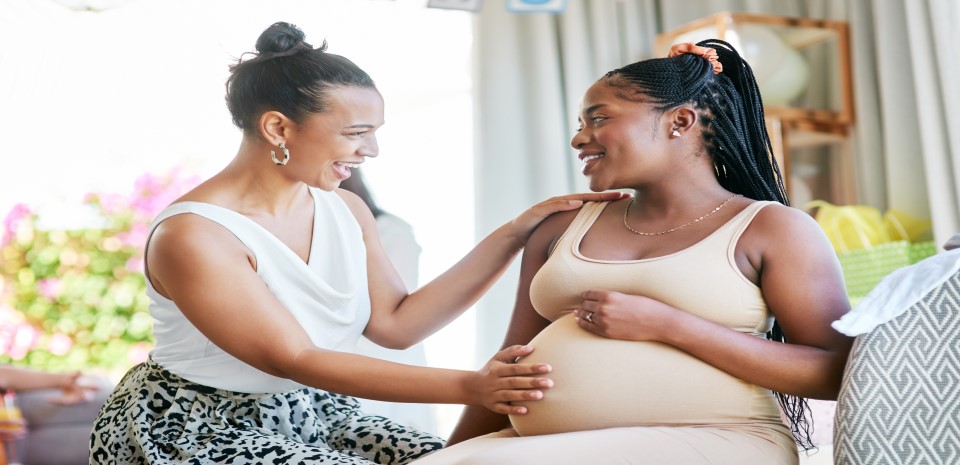 A black pregnant woman talking and smiling with her doula on a couch