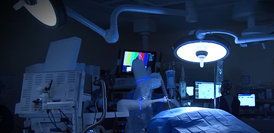 A dark operating room with someone seated in front a a computer screen in the background.