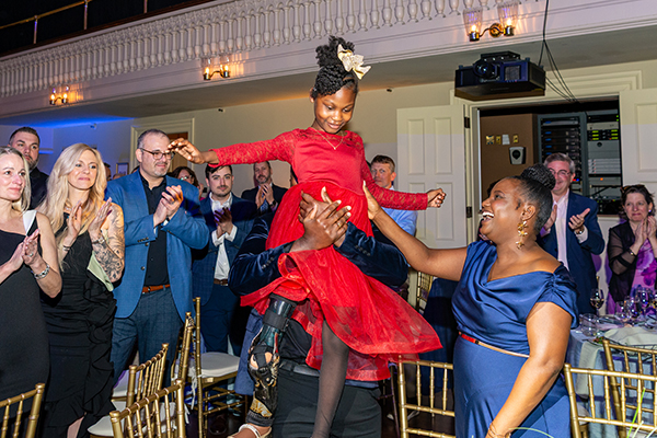 Young girl in red dress held up at table with people surrounding her.