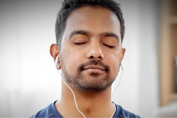 A man, with his eyes closed and wearing earbuds, practices mindfulness
