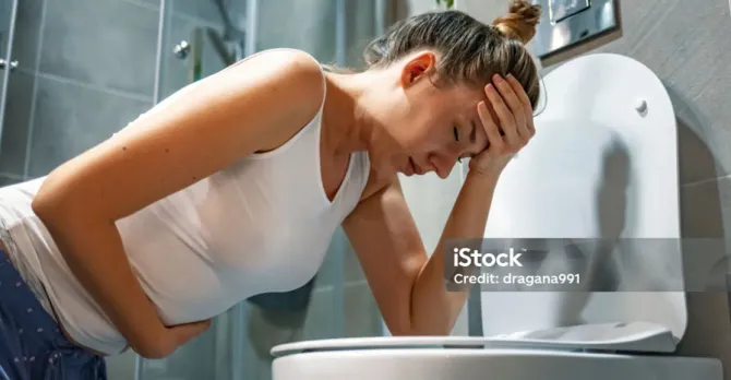 Woman in the early stages of pregnancy leans over the toilet expecting to vomit.