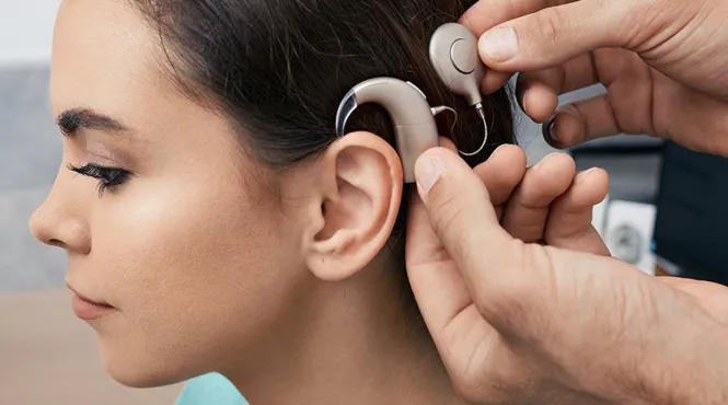 Having recovered from the cochlear implant surgery, a young female patient has her sound processor fitted behind her ear.