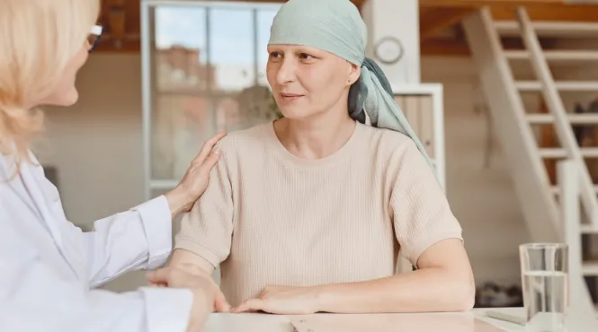 Woman with cancer wearing head cover is comforted by an oncology nurse navigator