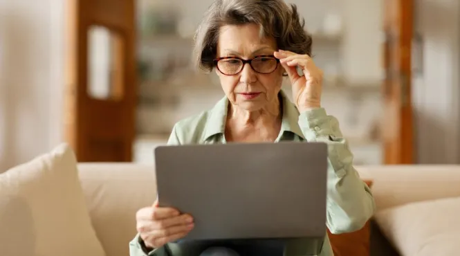 older woman with cataracts wearing glasses struggling to look at a computer.