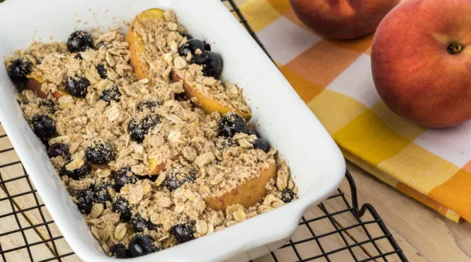 peach berry crisp cooling in a baking dish near fresh peaches