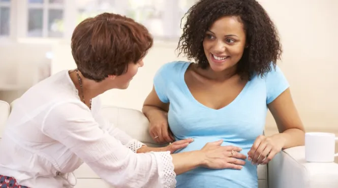 A doula with her hand on the tummy of a smiling pregnant woman on a couch