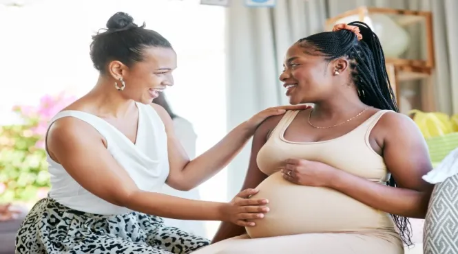 A black pregnant woman talking and smiling with her doula on a couch