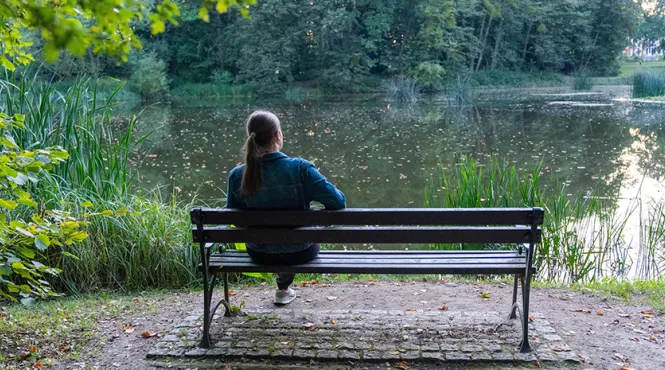 young woman sitting on bench near a pond