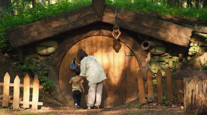 child and adult looking at a hobbit house in the woods.