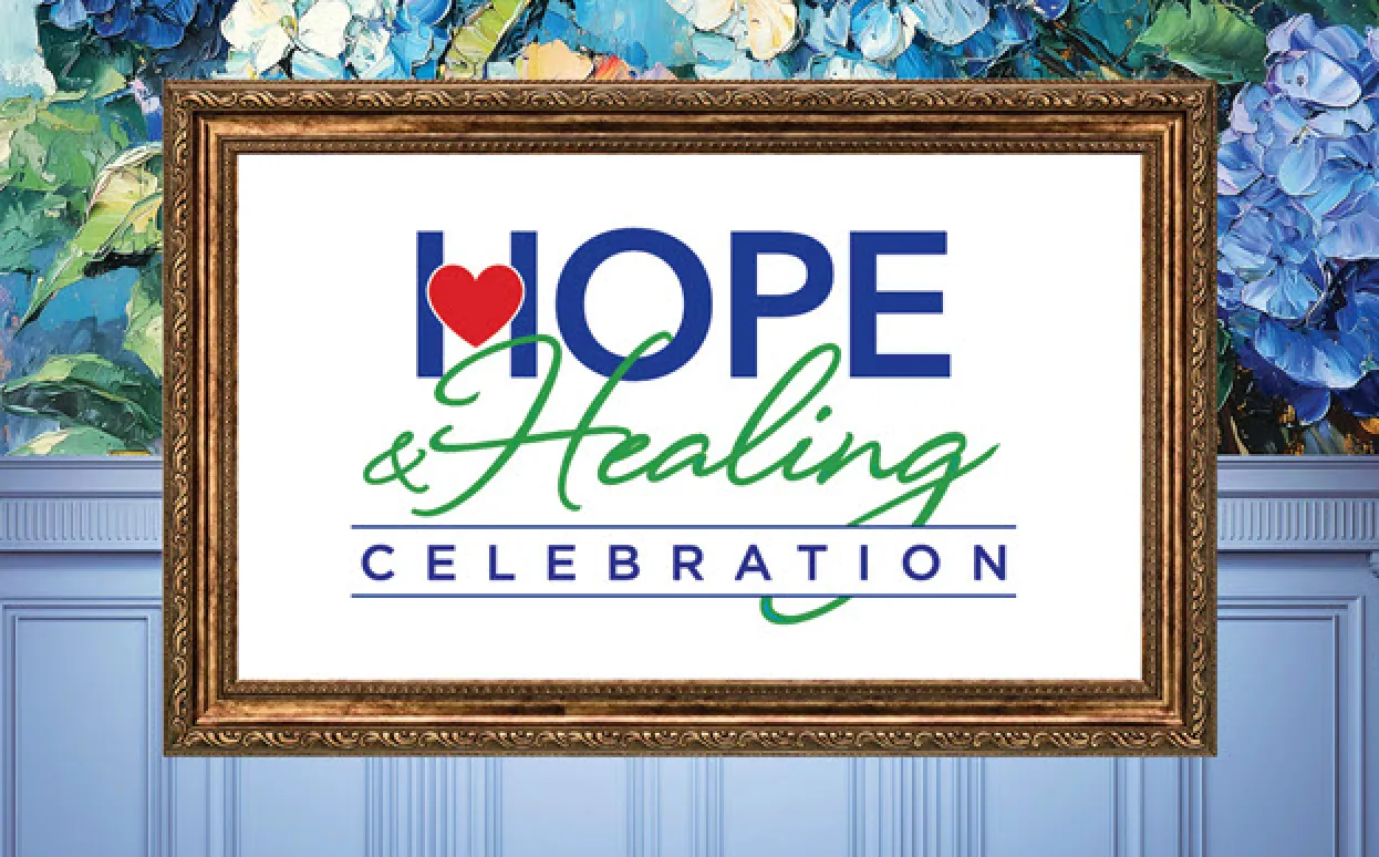 A golden picture frame on a wall with hydrangeas and wainscoting holds a sign for "Hope & Healing Celebration"