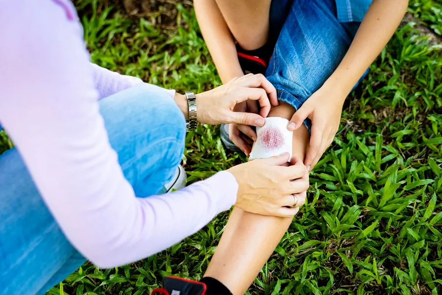 A woman's hands are holding some bandaging over a child's bloody knee.