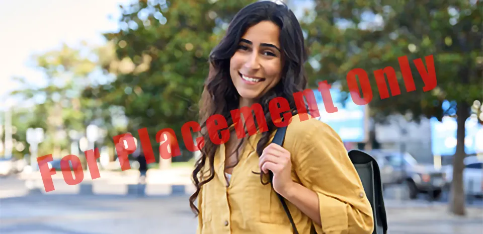 A young adult female, carrying a backpack, stands in a plaza and smiles toward the camera.