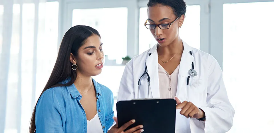 A patient looks on as her doctor shares information on a clipboard.