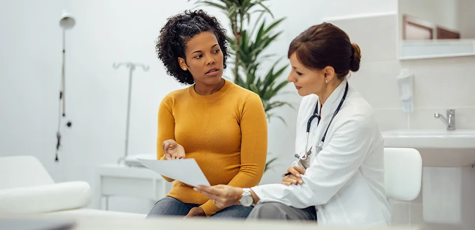 A woman in yellow discusses a document with her doctor.