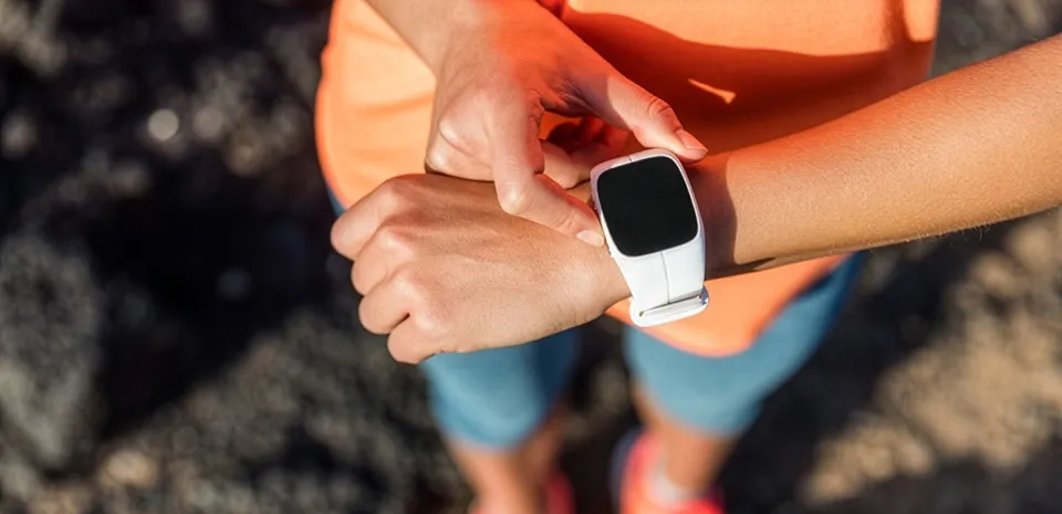 A woman looks at the fitness tracker on her wrist while walking outside.