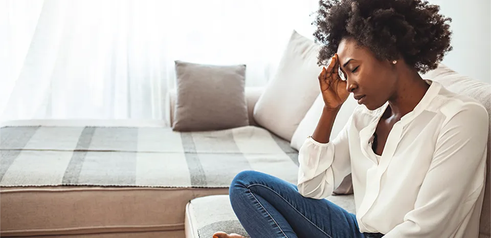 I black woman sitting cross-legged in a chair, hand on forehead and eyes closed.