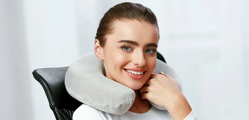 young woman sitting in chair with gray neck pillow around her neck