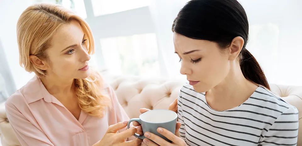 one woman consoling another and giving her a cup of tea in living room
