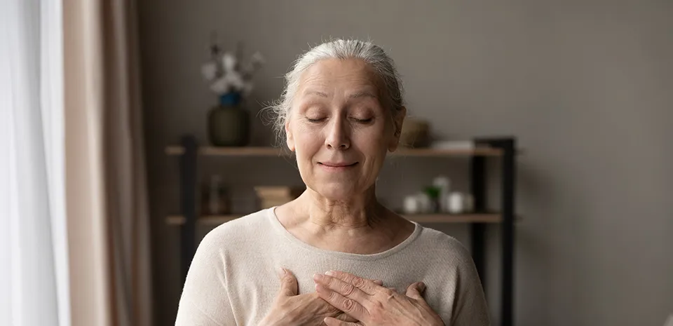 elderly woman mediating with hands over her heart