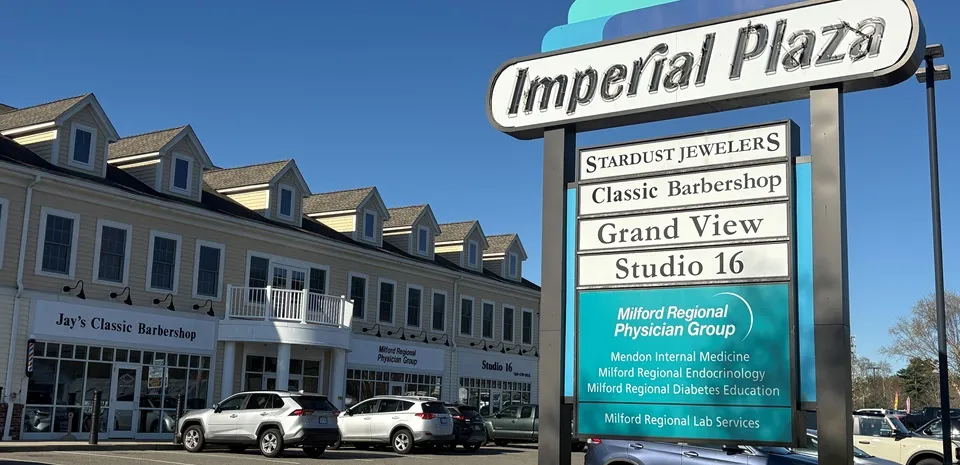 The Imperial Plaza in Mendon, Mass. The exterior of the while building has several cars in front. A sign reads "Milford Regional Physician Group."
