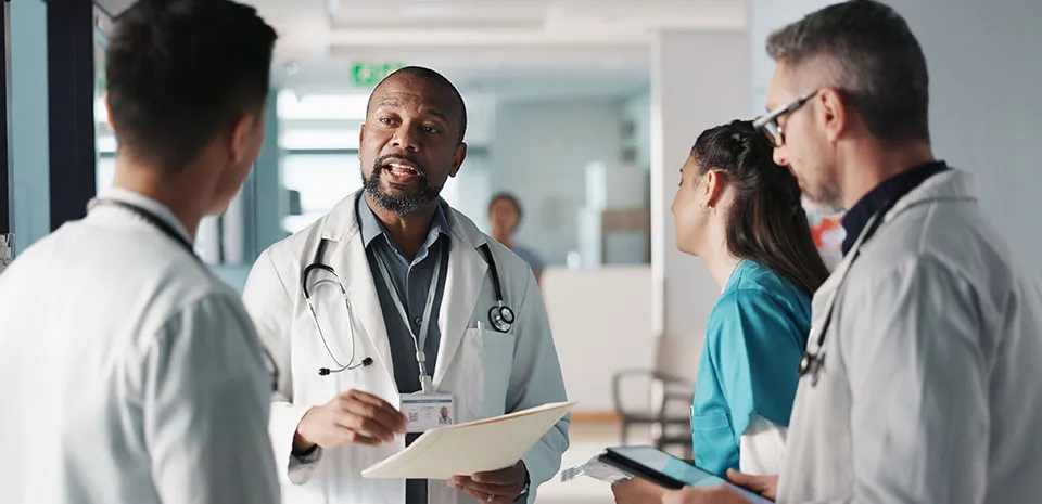 An experienced caregiver speaks to three students in training from an area in a hospital.