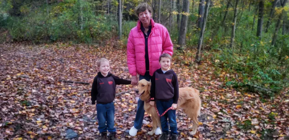 Female patient Jawan Betts stops to pose while on a walk in the woods with her two young grandsons and the family's golden retriever.