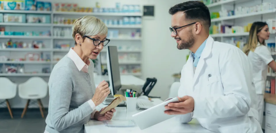 older woman talking to pharmacist about saving money on prescriptions