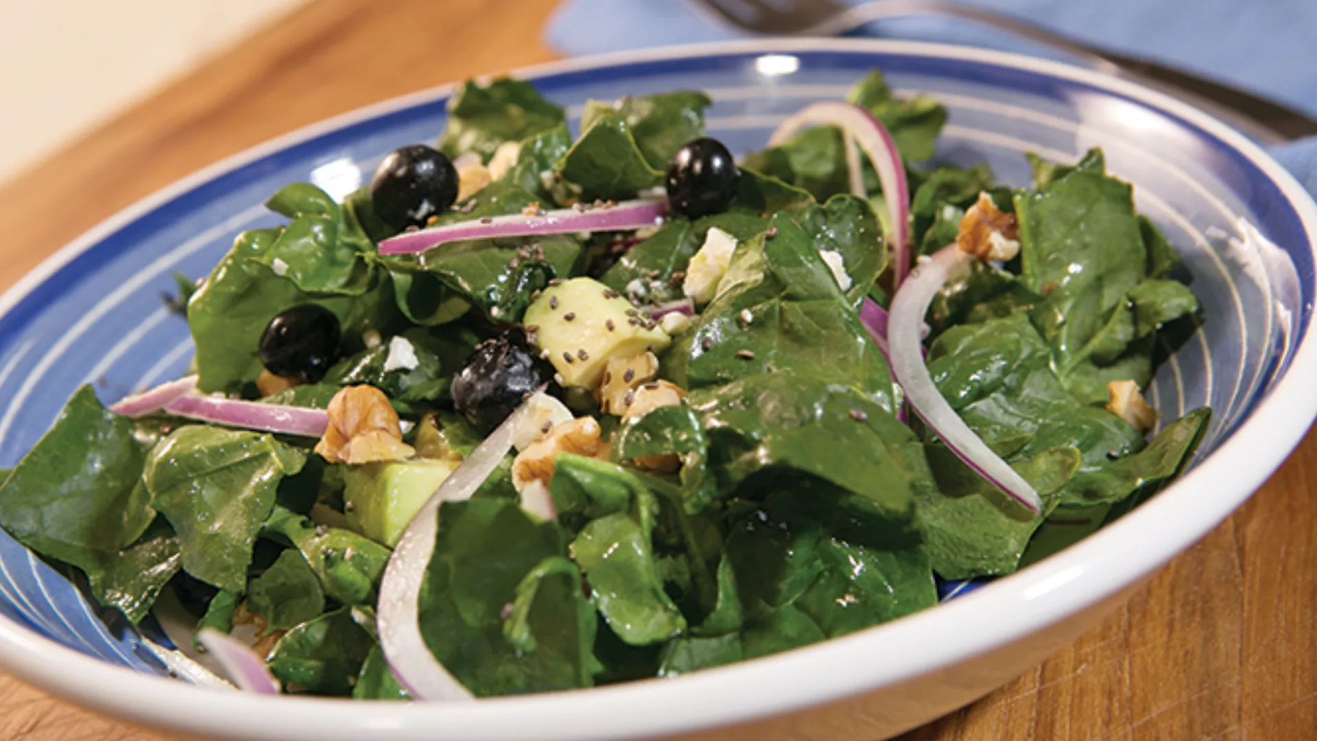 A blue bowl with a salad made of spinach, avocado, blueberries, onions, and chia seeds.