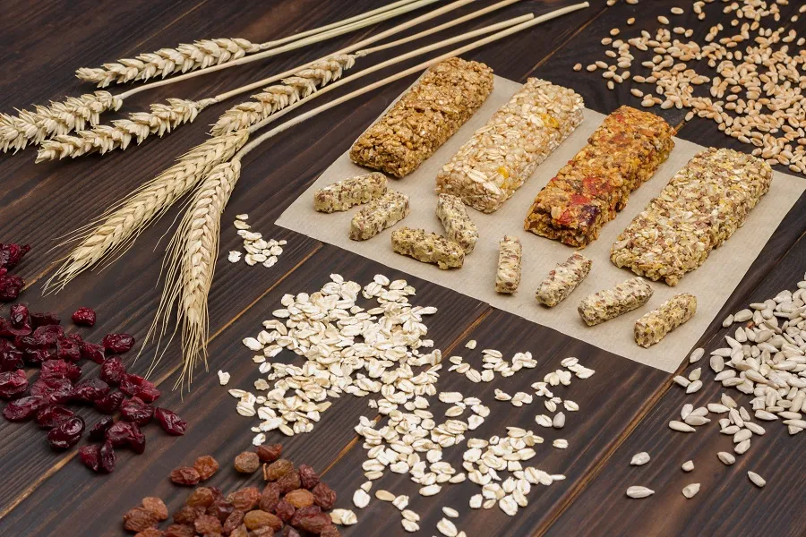 Multiple granola bars are on a table with various grains, oats, and wheat.