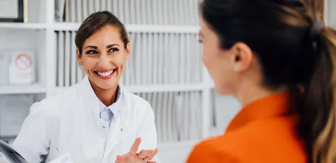 A hospital caregiver assists a patient who is standing at her station.