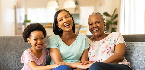 Three generations of females sit together on a sofa and share a laugh: mother, daughter, and grandmother.