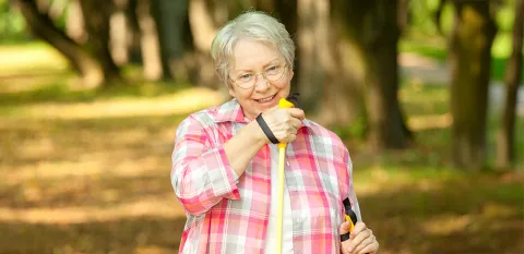 A senior woman uses walking sticks to prevent falls during her walk in the woods.
