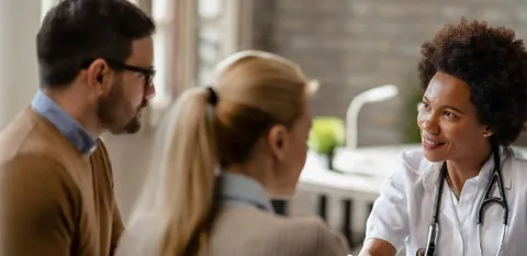A doctor meets with a couple and analyzes their medical test results on digital tablet during an appointment.