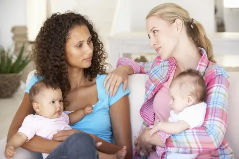 Two moms holding their babies, with one comforting the other