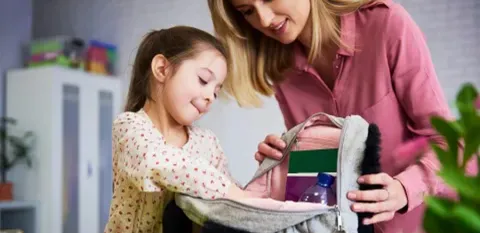 mom helping daughter pack backpack for school