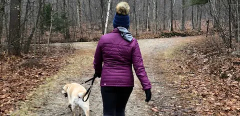woman walking dog down trail in woods