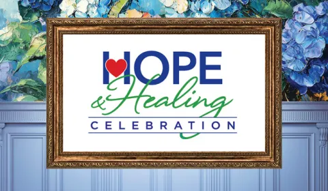 A golden picture frame on a wall with hydrangeas and wainscoting holds a sign for "Hope & Healing Celebration"