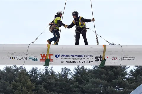 Construction workers on top of a large slab being hoisted onto the frame of the Nashoba emergency facility.
