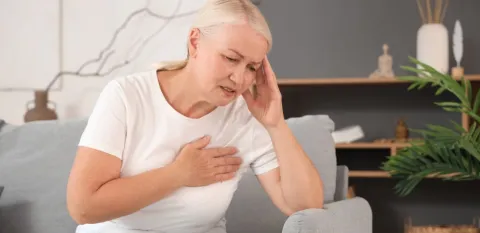 woman on couch holding sore arm caused by lymphedema after cancer.