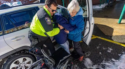 A Dennis police officer helps Barbara Cormier lift her 91-year old mother into a wheelchair as they arrive at the emergency shelter set up at the Dennis Yarmouth Regional High School for victims without heat or power. 