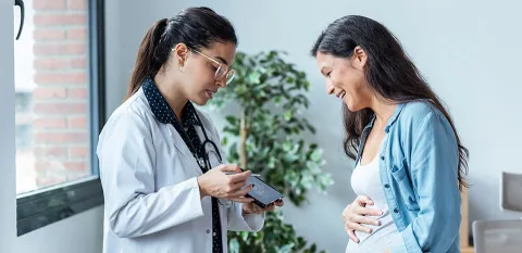 A doctor on the left showing a patient on the right a picture of an ultrasound. The patient on the right holds her stomach, smiling at the ultrasound.