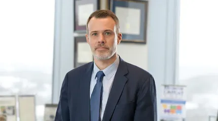 Dr. David McManus, the next chancellor of UMass Chan Medical School wears a suite and tie in an office that overlooks the landscape.
