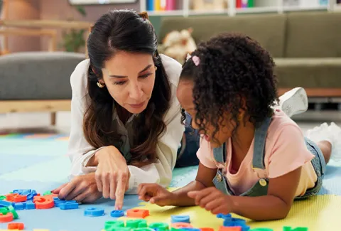 Child Life specialist laying on the floor pointing to alphabet letters with a young black child right next to her