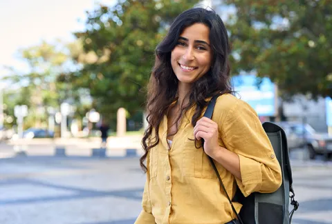 Student intern with long, dark, wavy hair wearing a mustard yellow button-up dress shirt with a backback over her shoulder