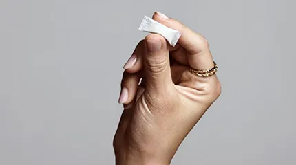 A caffeine pouch is being held between the thumb and forefinger of a woman's hand.