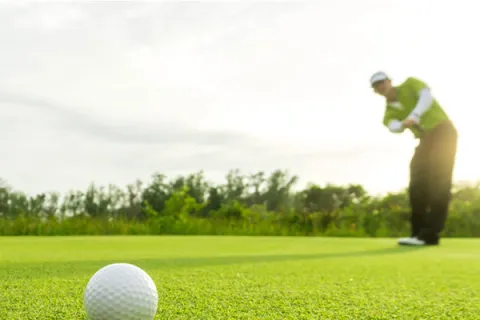 A golf ball sits on the green while a golfer watches from further away.