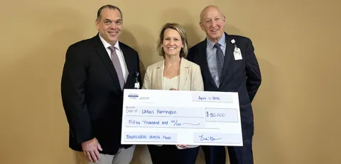 Erika Burros, representing the auxiliary, holds a large-sized donation check.  To her sides stand Harrington Board of Trustees member and the President of the Center of Hope Foundation.
