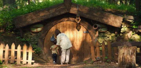 child and adult looking at a hobbit house in the woods.
